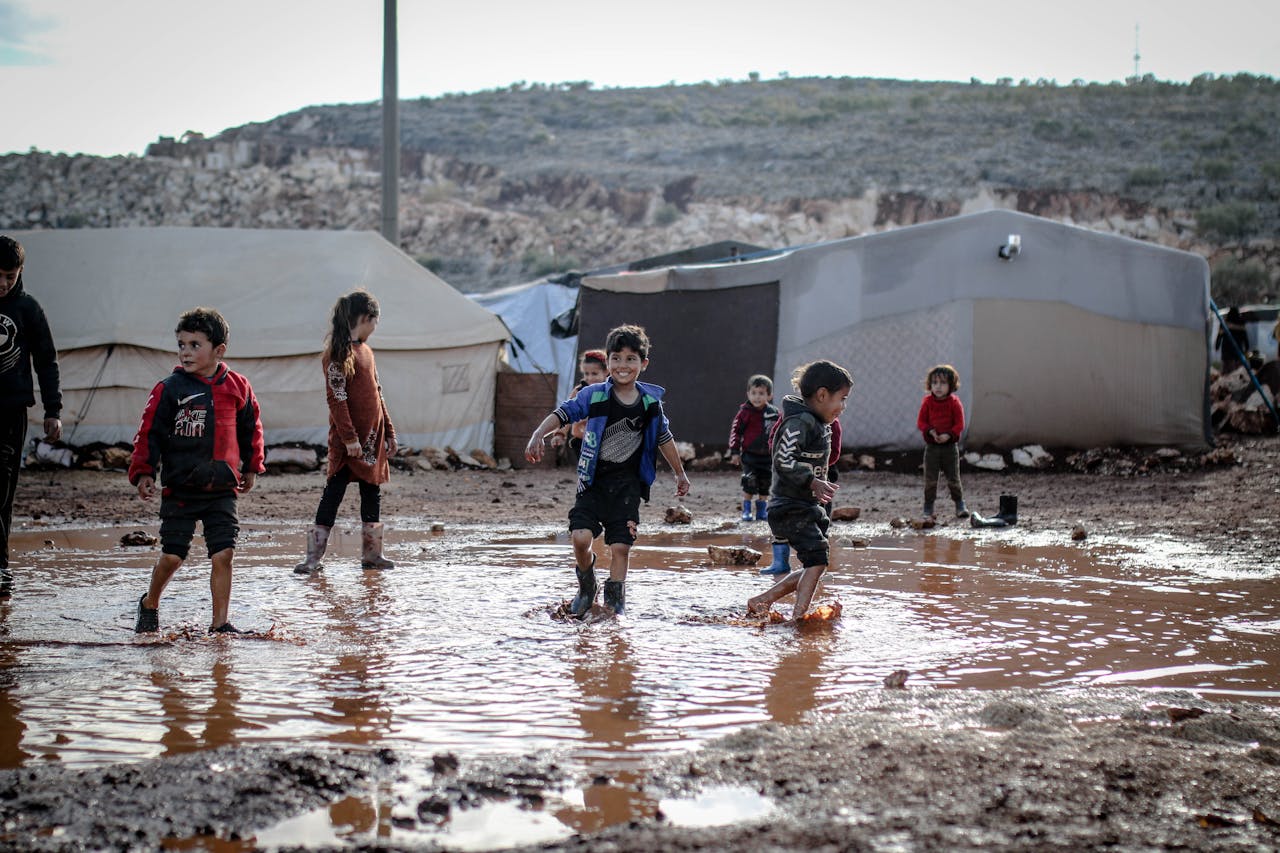 services-01 Kids enjoying playtime in a muddy refugee camp in Idlib, Syria amidst challenging conditions.