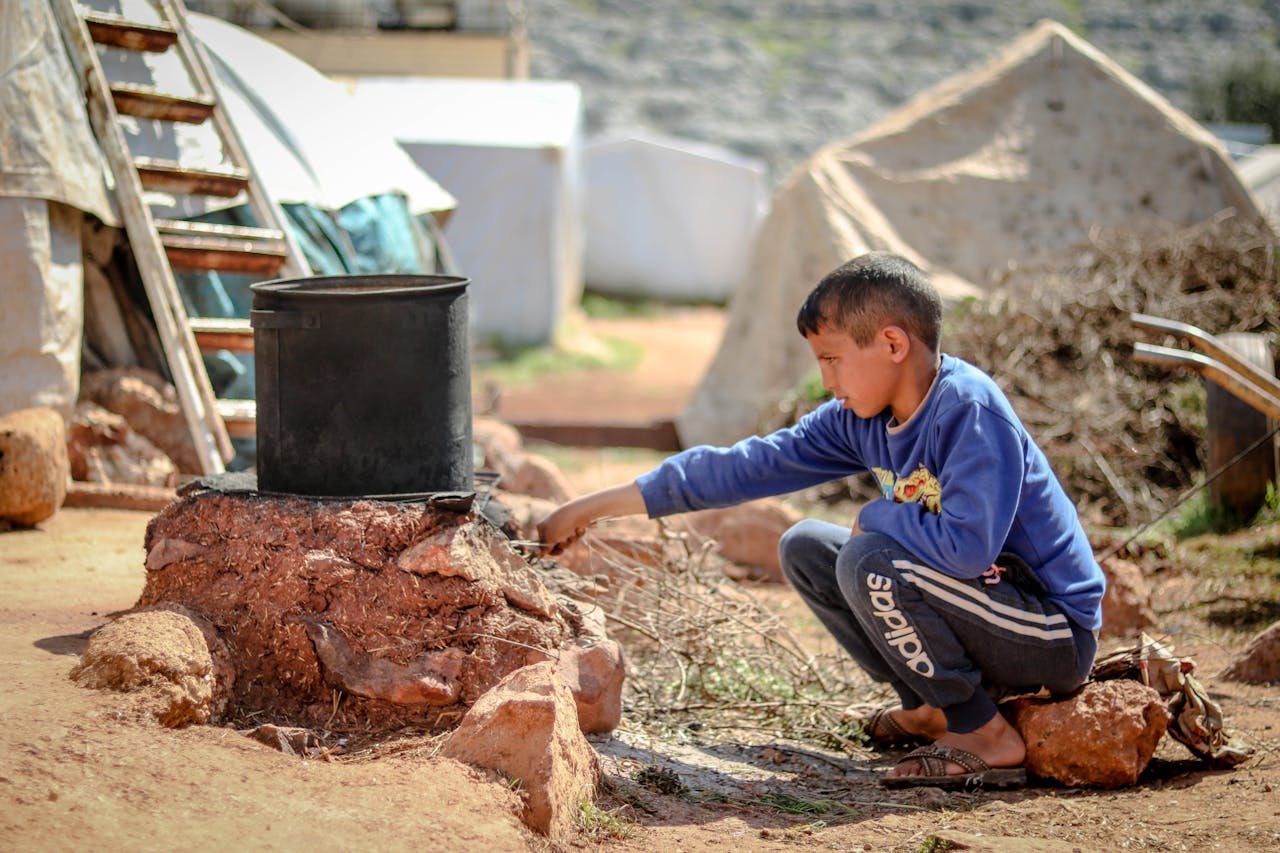 heros-img A young boy tends to a cooking pot outdoors in a refugee camp in Idlib, Syria.