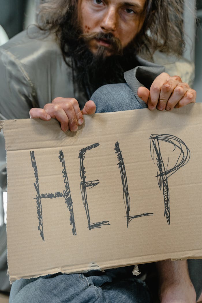 about-us A homeless man holding a cardboard sign with 'HELP' written on it, expressing need.