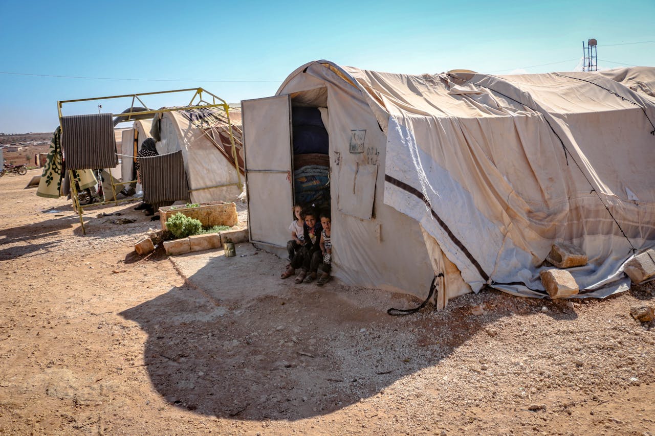 Young children standing near tents in a refugee camp in Idlib, Syria. Focus on poverty and displacement.